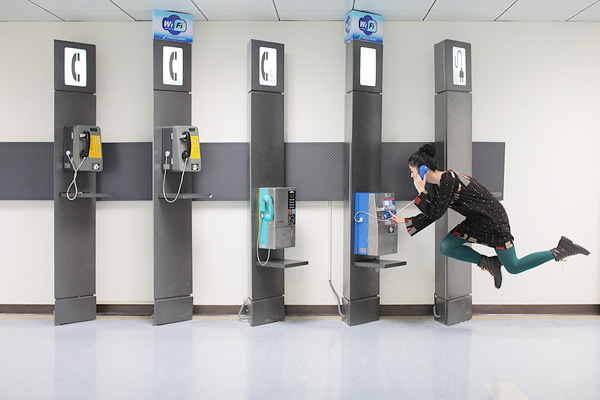 公衆電話で浮遊して電話をする女性の写真